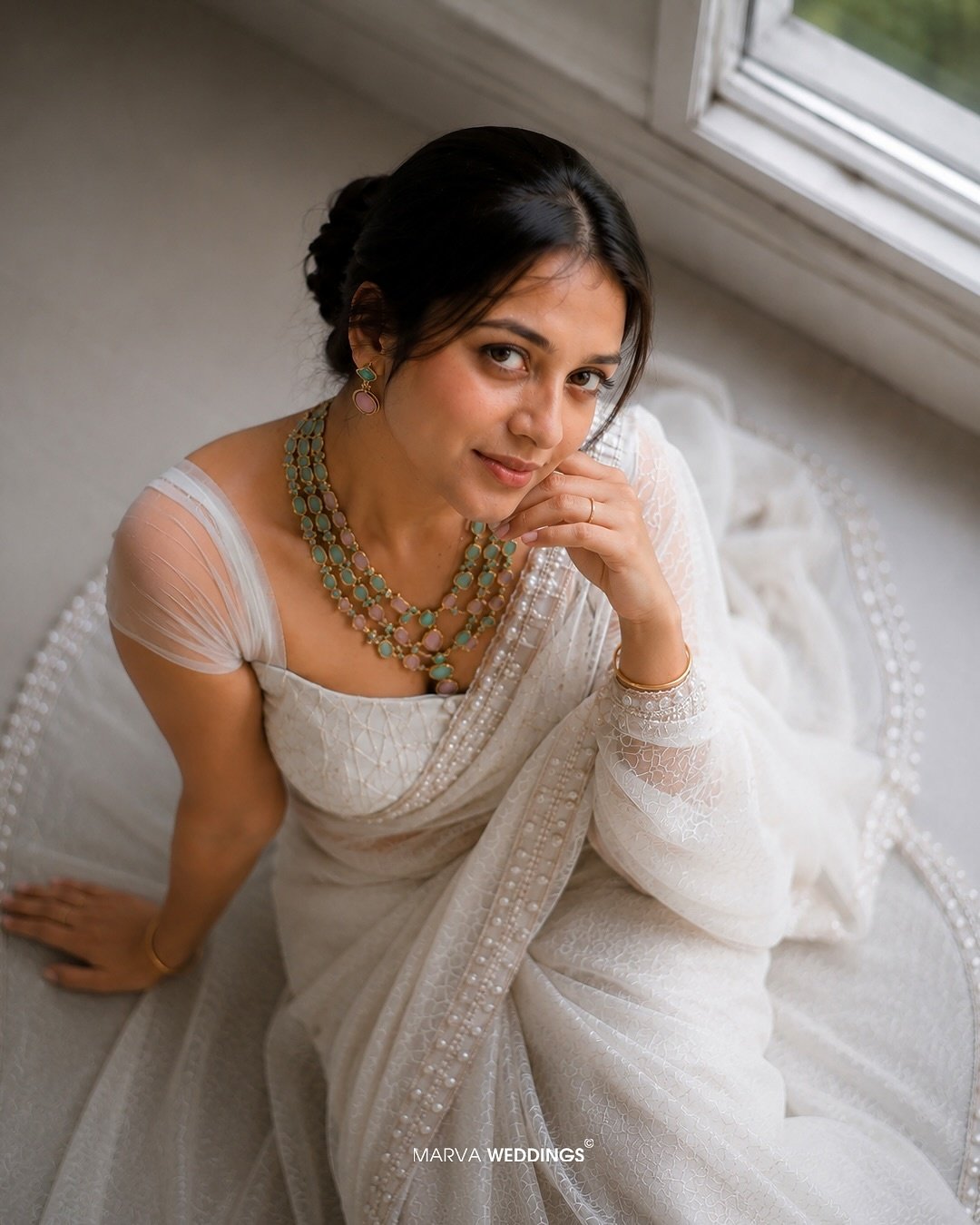 Bride in a white sari seated beside a softly lit window